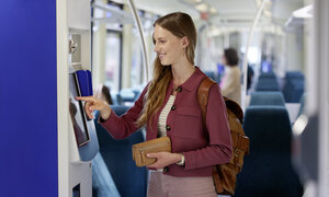 Eine Frau die in einer Tram ein Ticket am Ticketautomaten kauft.