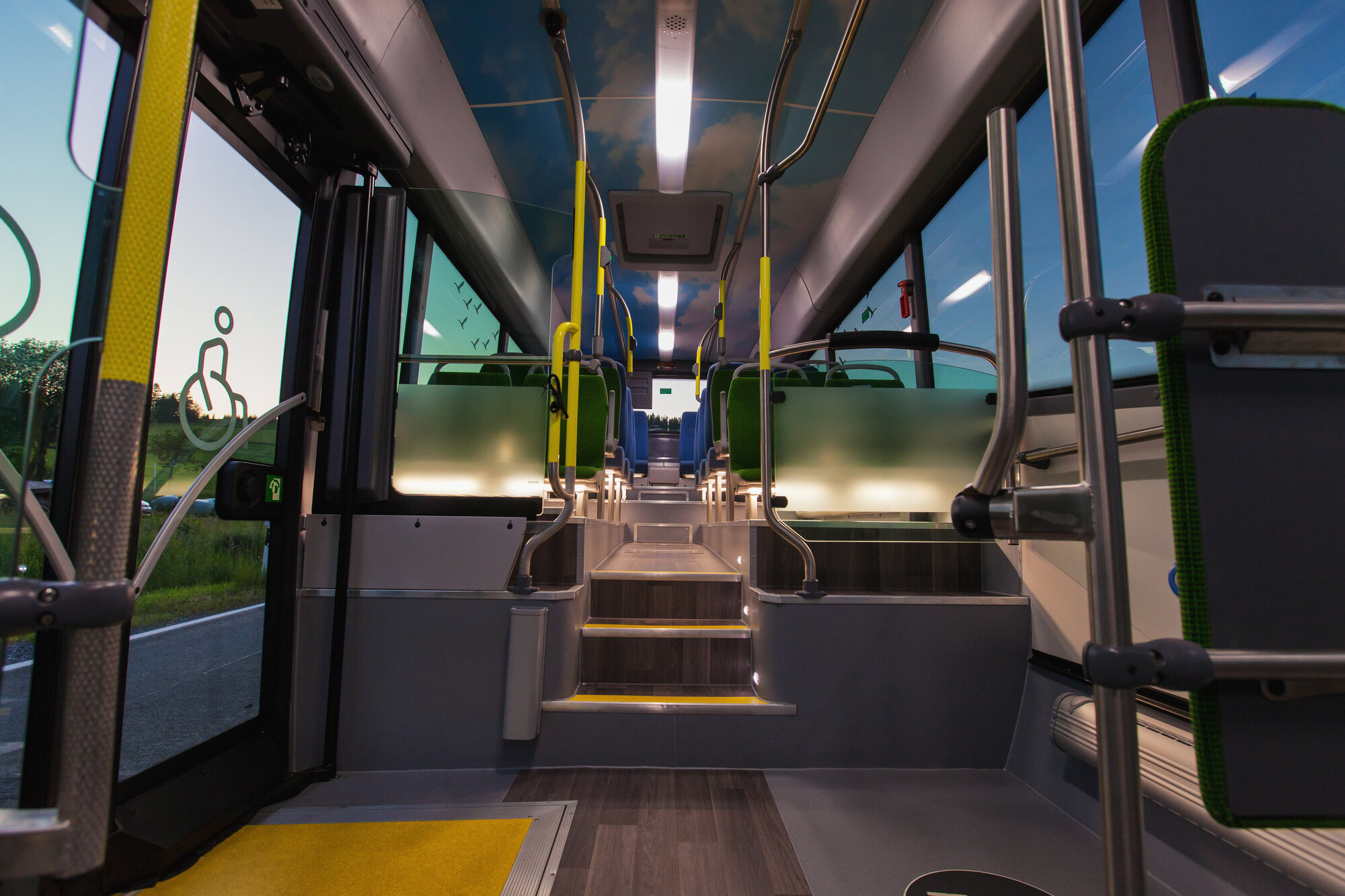 Der beleuchtete Innenraum eines Busses mit Blick von vorne nach hinten auf die Seitzreihen und Stufen.